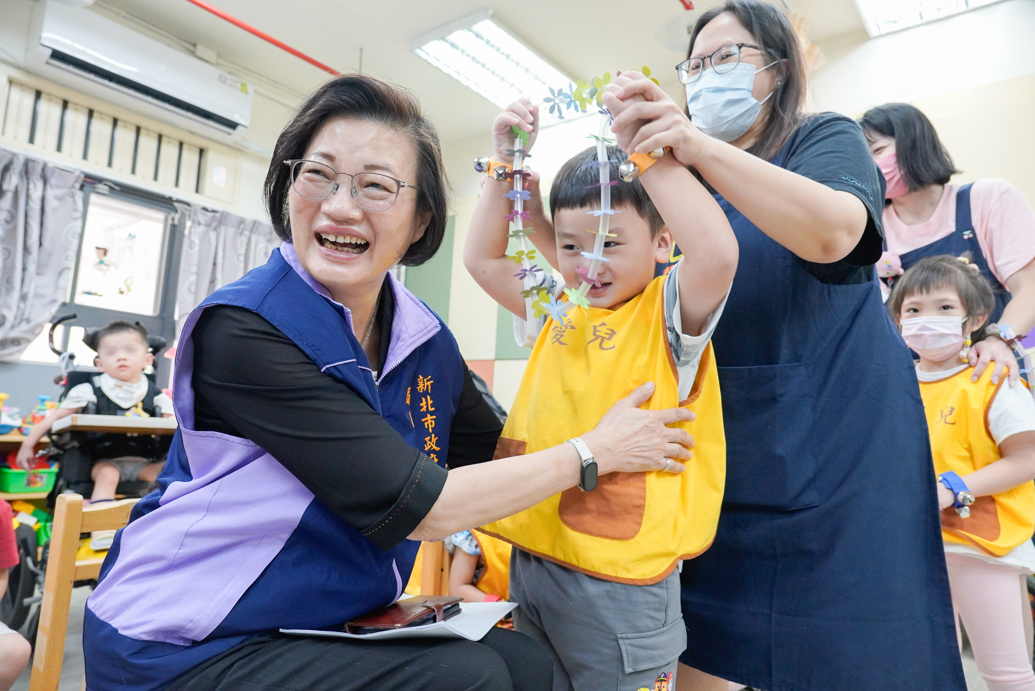 新北社會局長李美珍慰訪愛兒等7家機構 代表市長致贈秋節加菜金及蘋果 7 愛兒兒發中心的威威要代表中心獻上自製的小花環給李美珍局長卻直往自己脖子套惹得眾人笑彎了腰